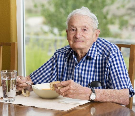 Oudere man eet soep en brood