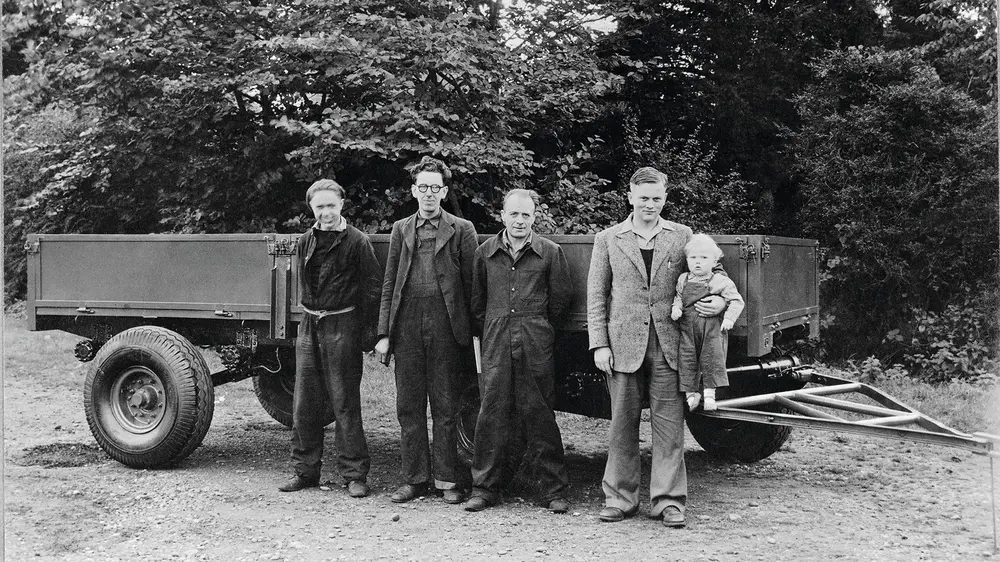 1947 - Anthony Bamford in de arm van zijn vader. Van links naar rechts werknemers Bill Hirst, Arthur Harrison en Bert Holmes