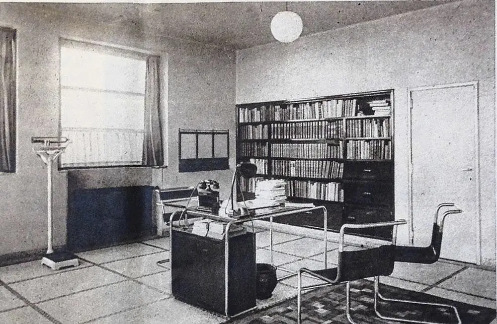 Interieur van de spreekkamer met ingebouwde bibliotheek, typische granito vloeren en buismeubelen.