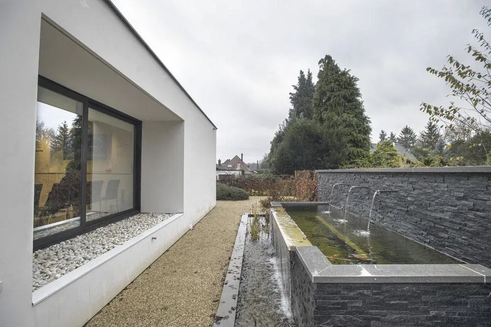 De vloeiende lijnen van de tuin, met daarin de brede waterval, contrasteren met de strakke rechte lijnen van het huis.
