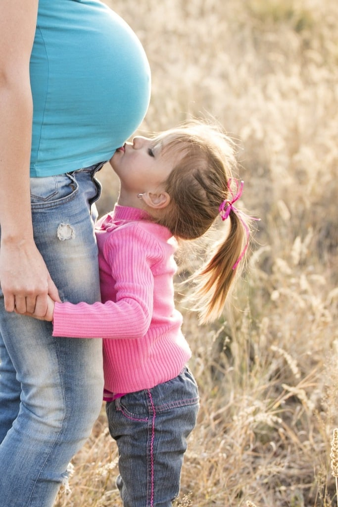 kid kissing pregnant woman in a field