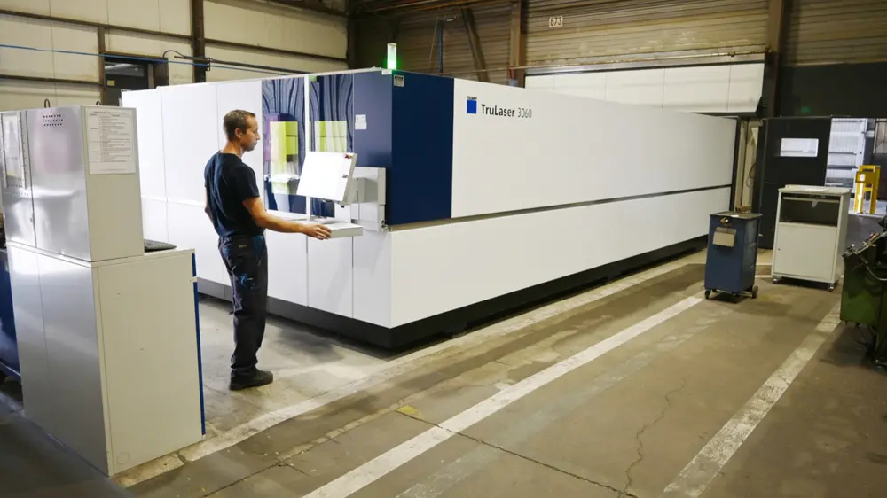 Le panneau de commande de la découpeuse laser fibre se trouve dans un hall de production, la table de charge dans un autre